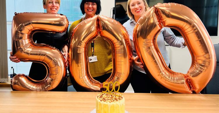 Three women with balloons in the shape of the number 500