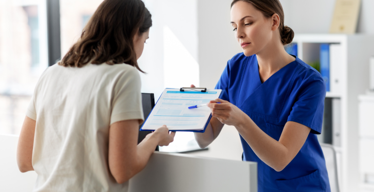 female hospital receptionist handing clipboard to female patient