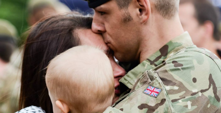 A soldier in army uniform, embracing his partner and child.