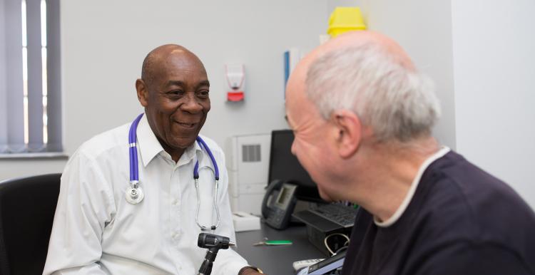 GP speaking to a patient, about to use a thermometer