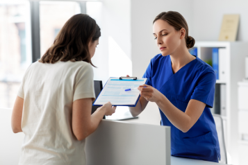 female hospital receptionist handing clipboard to female patient
