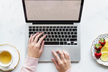 person using laptop with teacup and plate of fruits