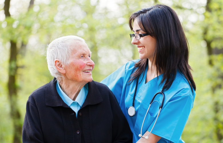 older patient with female nurse standing outside in front of trees