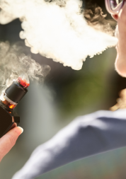 Over the shoulder view of a woman smoking an electronic cigarette or vape outdoors.